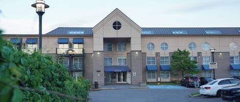 A modern hotel with a reception area, parking lot, and a building with multiple windows and a blue awning.