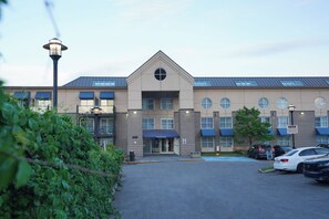 A modern hotel with a reception area, parking lot, and a building with multiple windows and a blue awning. - Hôtel Lindbergh par JARO (Québec City)