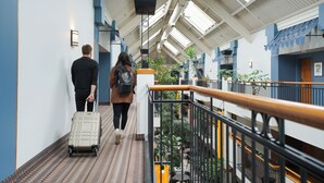 A corridor with a tiled floor, a metal railing, and a staircase leading to an upper level. - Hôtel Lindbergh par JARO (Québec City)