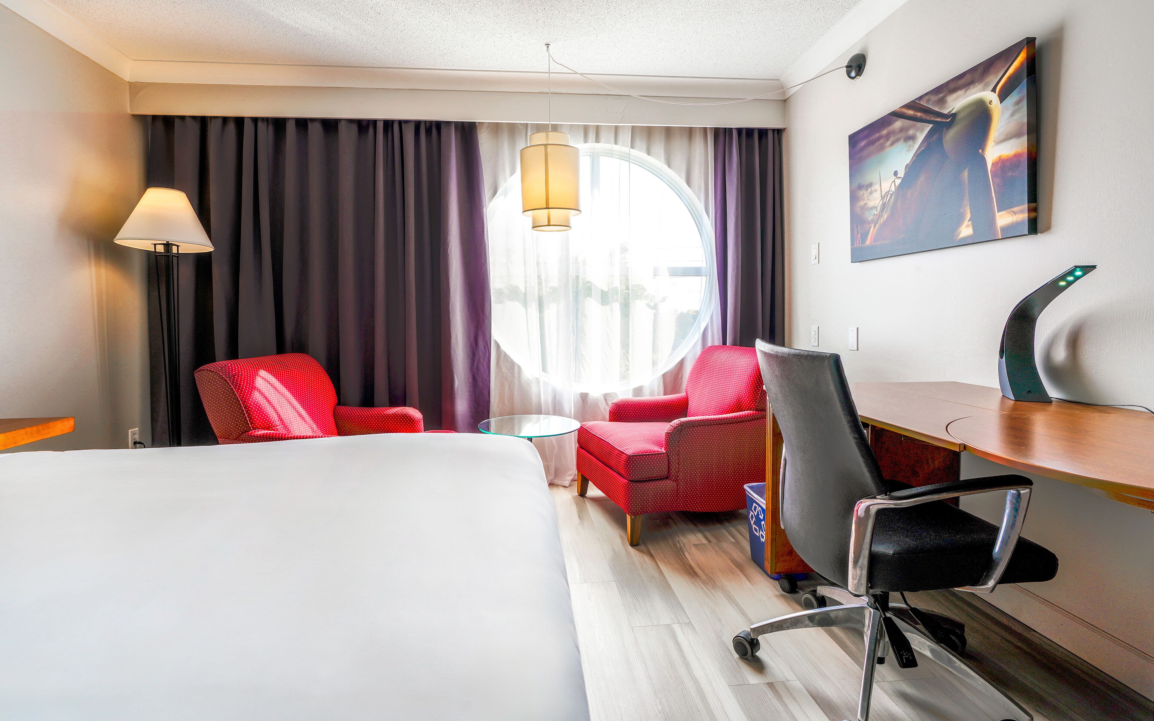 Una habitació d'hotel amb un llit, escriptori, dues cadires, una làmpada i un quadre a la paret.