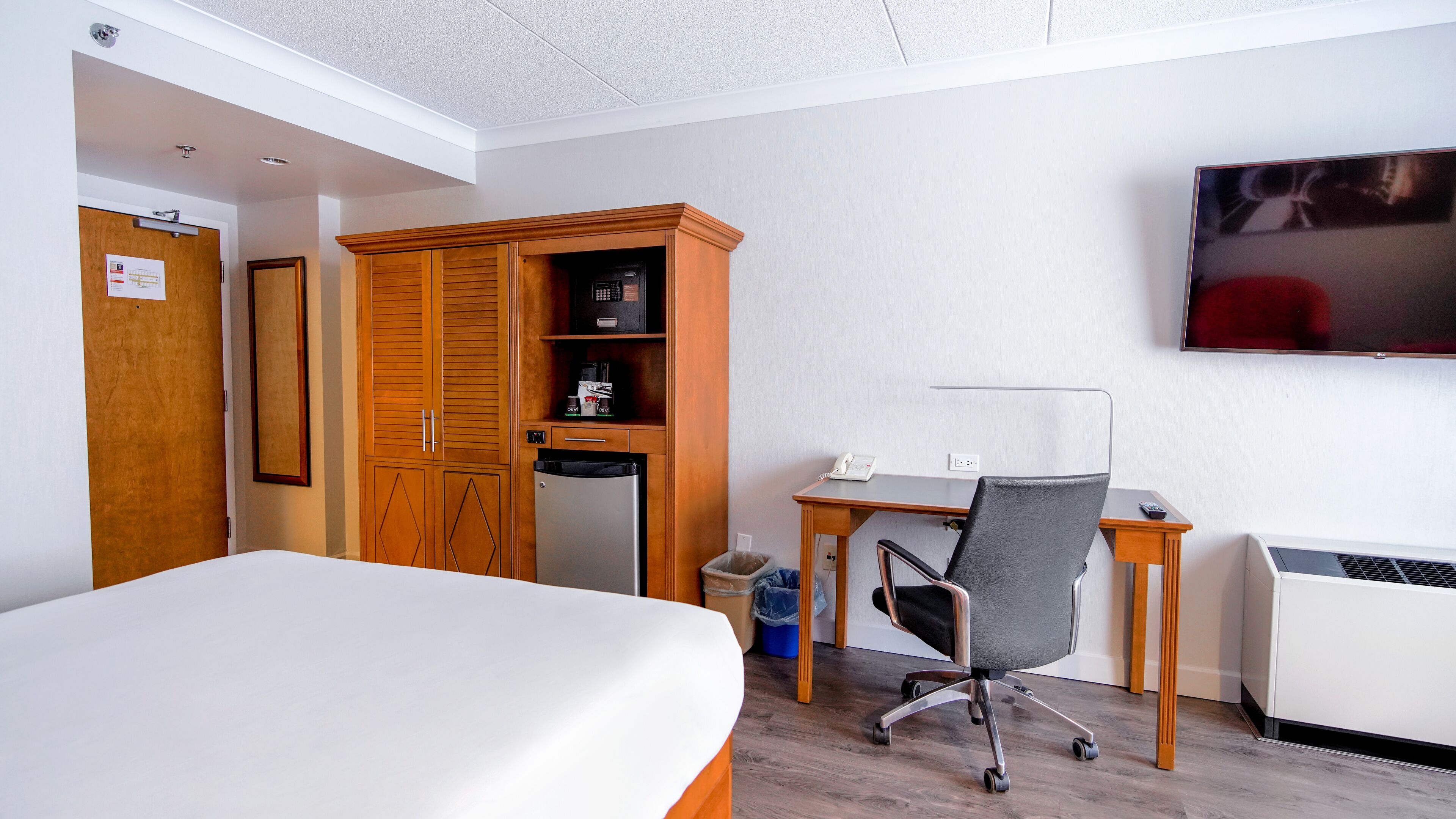Una habitación de hotel con cama, escritorio con silla, televisor, armario y basurero.