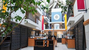 A modern atrium with a central kitchen area, multiple floors, and a decorative clock. - Hôtel Lindbergh par JARO (Québec City)