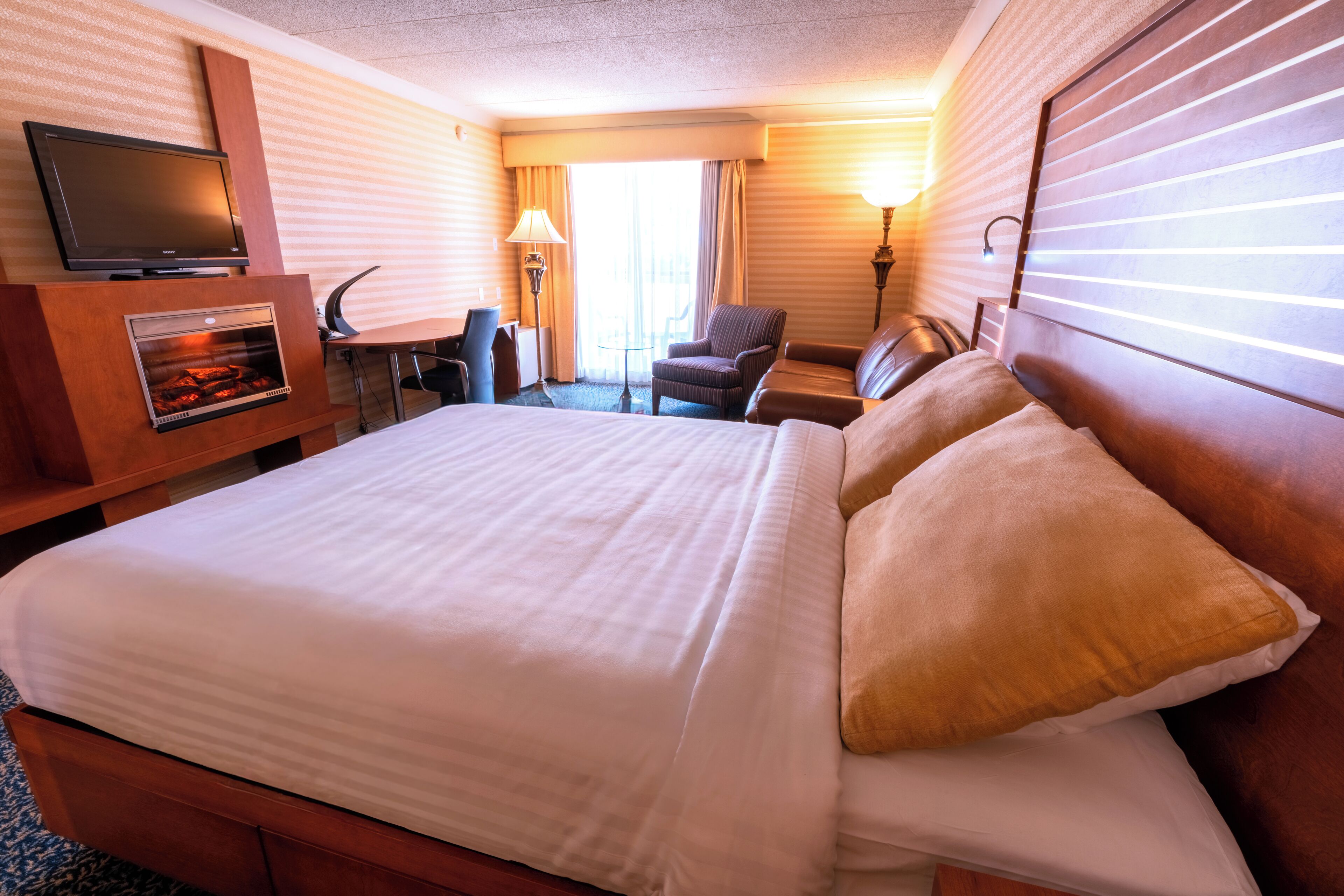 Una habitación de hotel con cama, televisión, chimenea, escritorio y una silla.