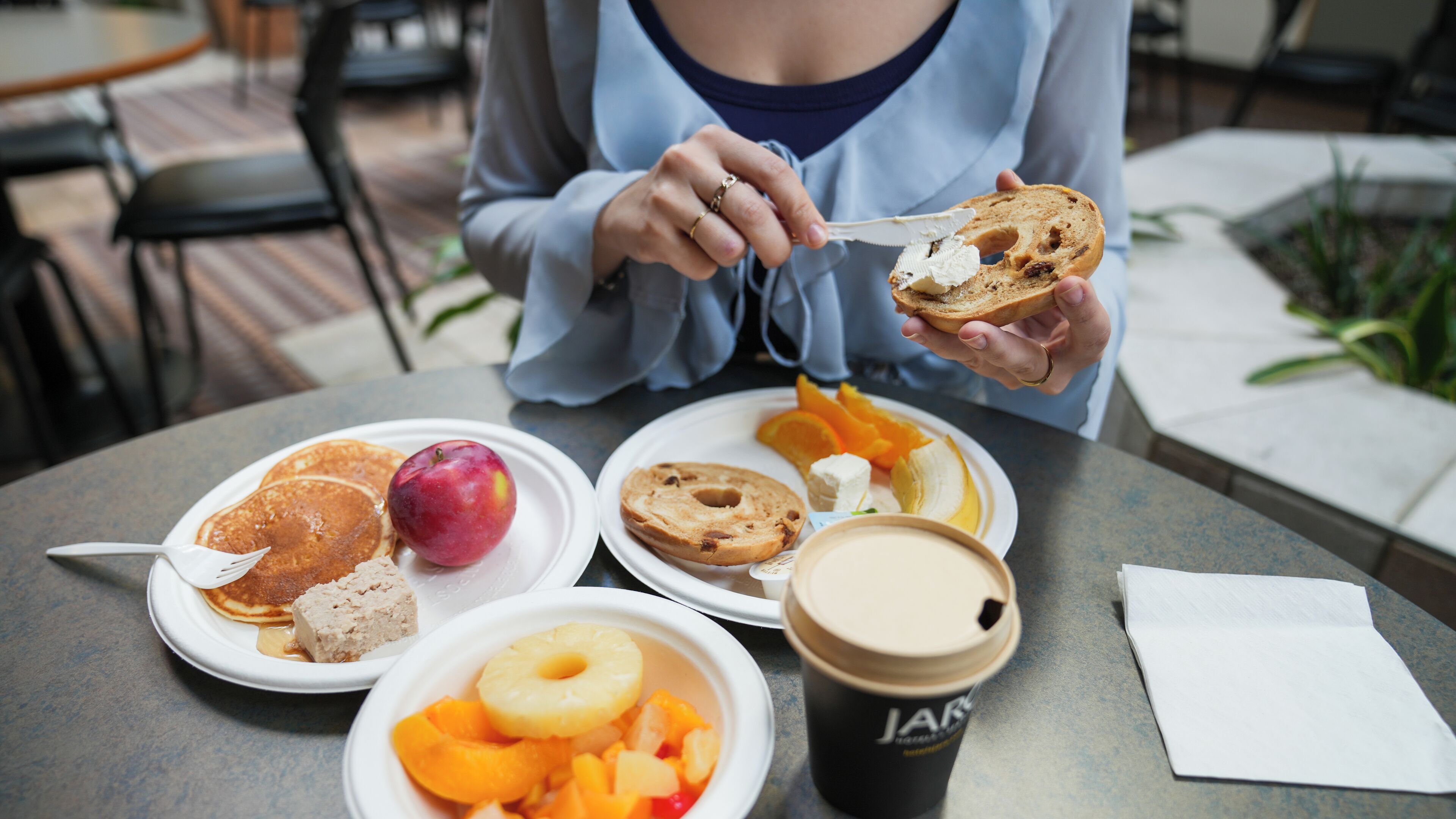 A person eating breakfast at an outdoor table with plates of food, a coffee cup, and a napkin.