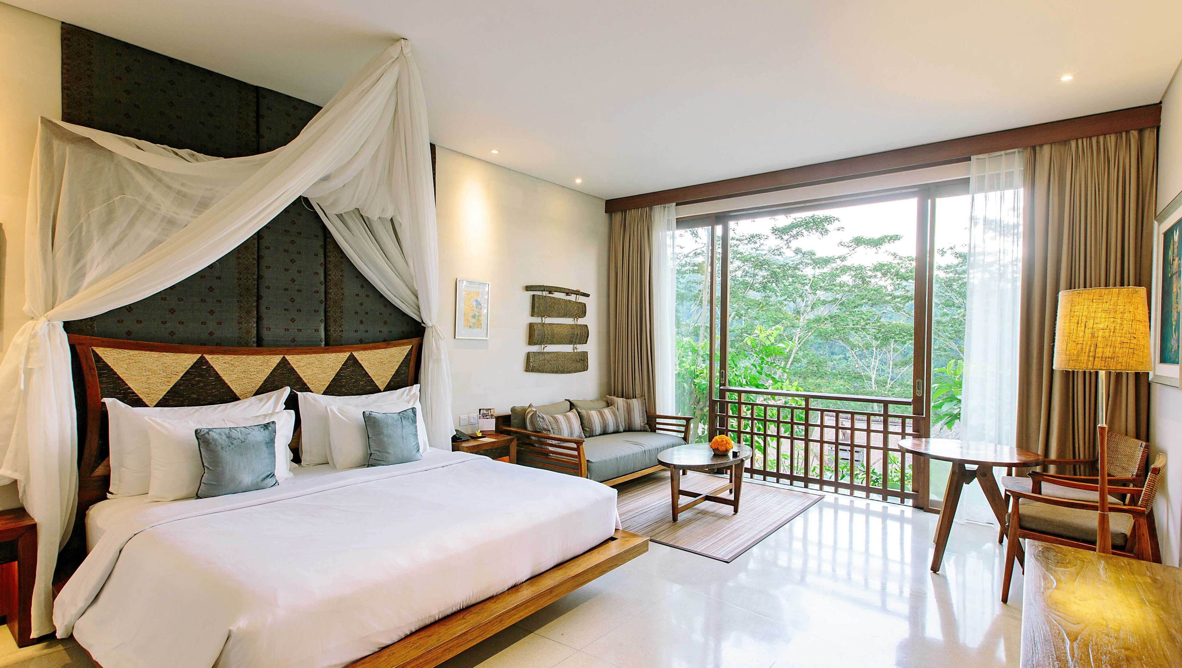 Quarto com cama grande, sofá, mesa pequena e varanda com vista.