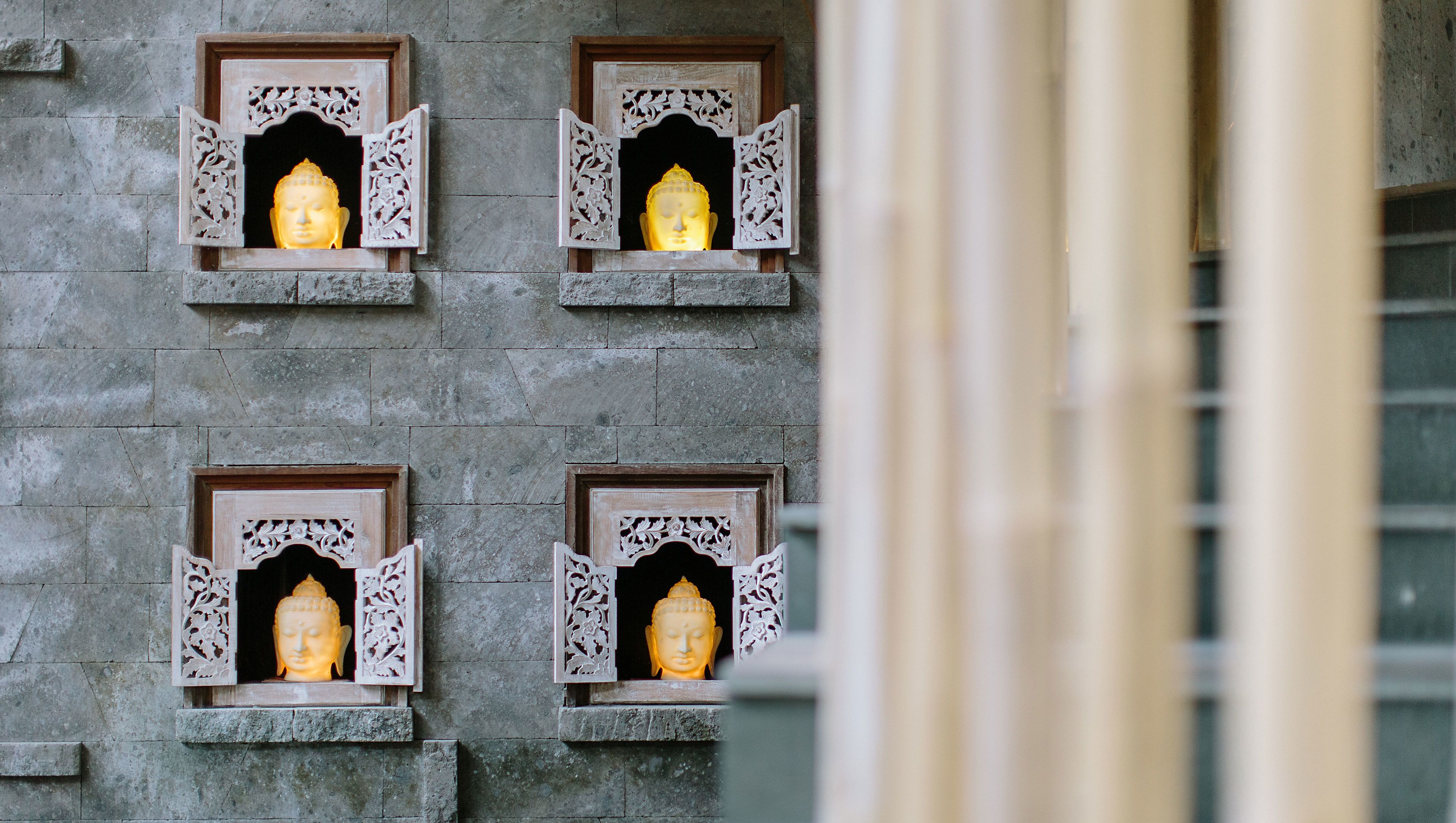 Four illuminated Buddha statues in ornate wooden frames against a stone wall.