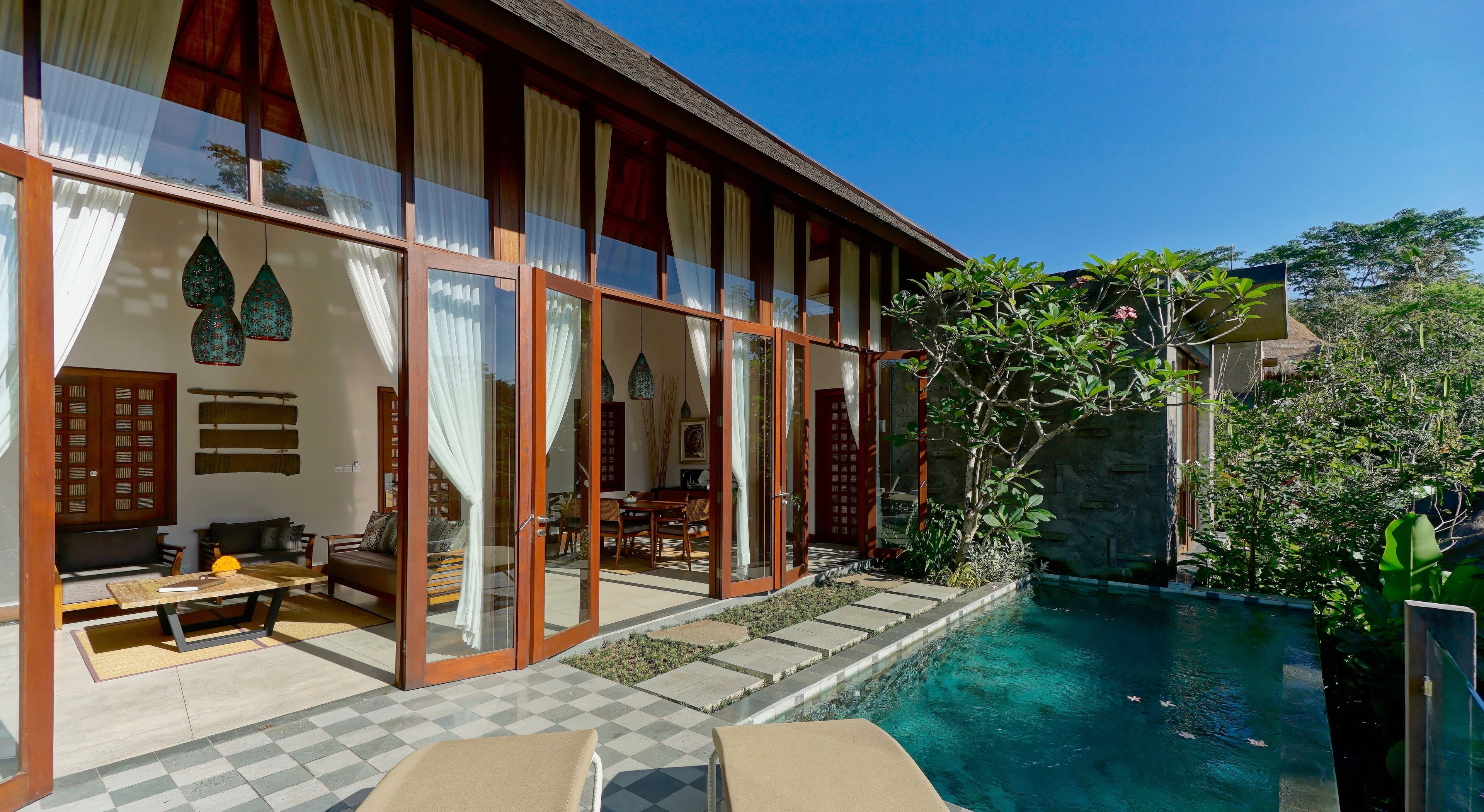 A modern villa with a pool, large glass doors, and a dining area.