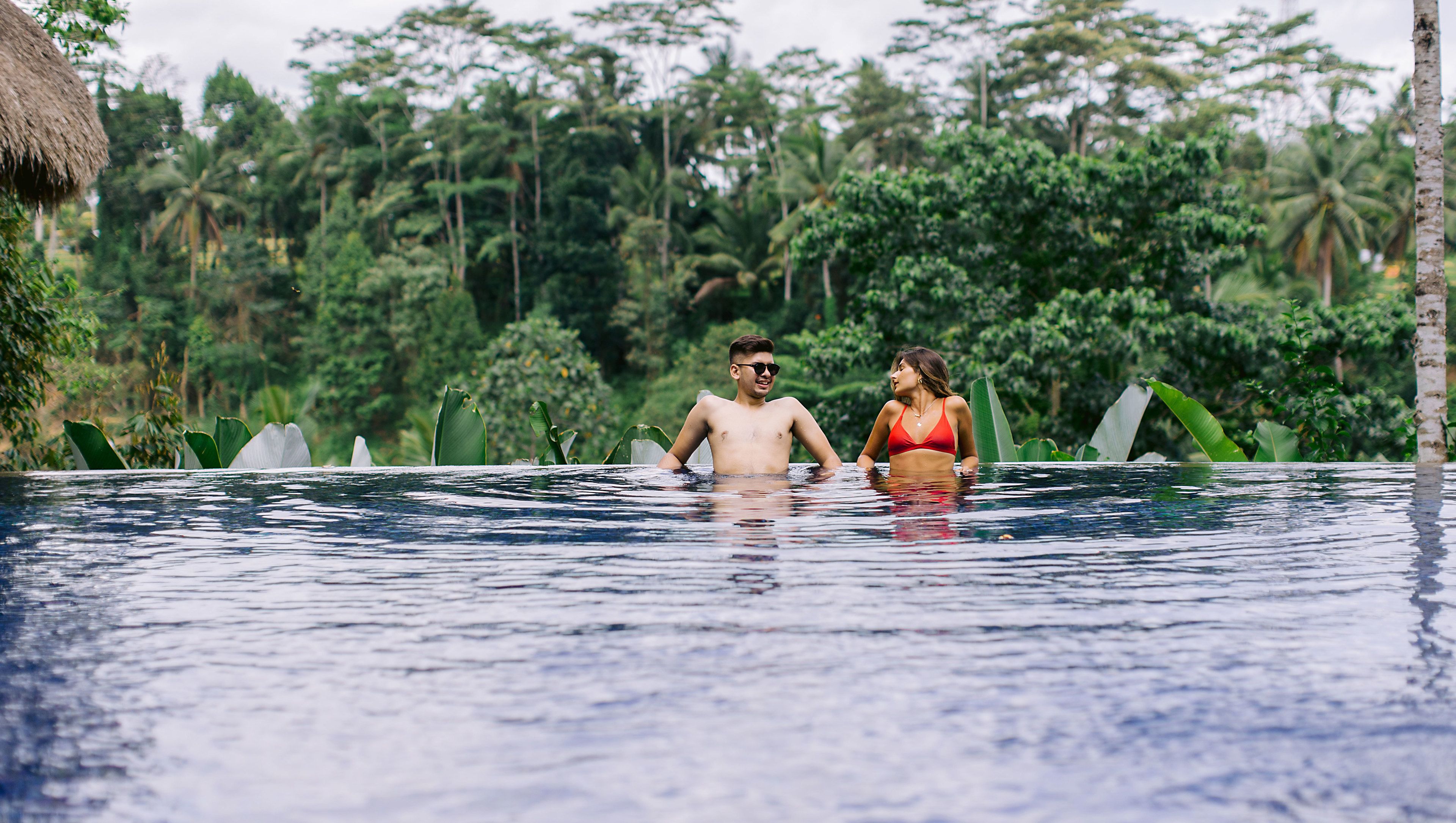 A couple in a swimming pool surrounded by lush greenery.