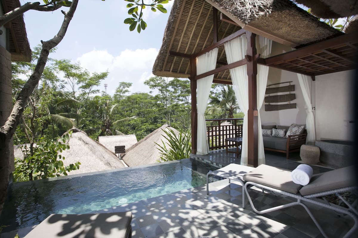 A pool area with a lounge chair, a thatched-roof structure, and a view of the surrounding greenery.