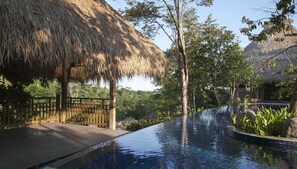 A poolside area with a thatched-roof structure, wooden deck, and lush greenery. - Tejaprana Resort & Spa (Ubud)