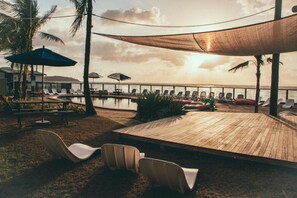 A wooden deck with lounge chairs and umbrellas, overlooking a pool and ocean view. - Base Backpackers Magnetic Island - Hostel (Nelly Bay)