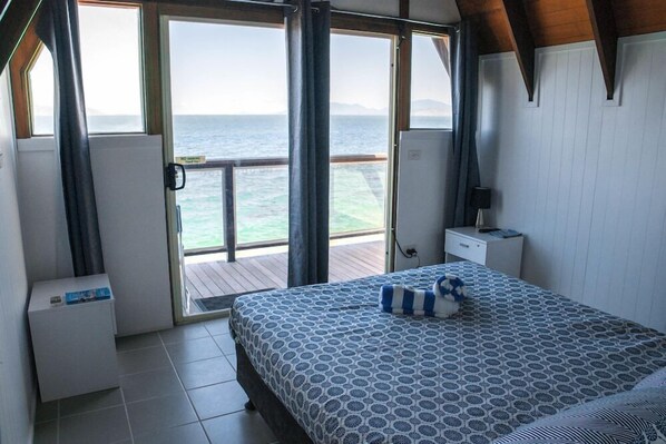 A bedroom with a large bed, a nightstand, a dresser, and a view of the sea through open doors. - Base Backpackers Magnetic Island - Hostel (Nelly Bay)