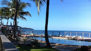 A poolside area with lounge chairs, palm trees, and a view of the ocean. - Base Backpackers Magnetic Island - Hostel (Nelly Bay)