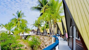 A coastal hotel with a balcony, palm trees, and a rocky shoreline. - Base Backpackers Magnetic Island - Hostel (Nelly Bay)
