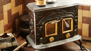 A vintage stove with a metal pot on top, a small metal container with a handle, and a brick wall with a checkered pattern. - Pension Hoshi Ni Negaiwo (Furano)