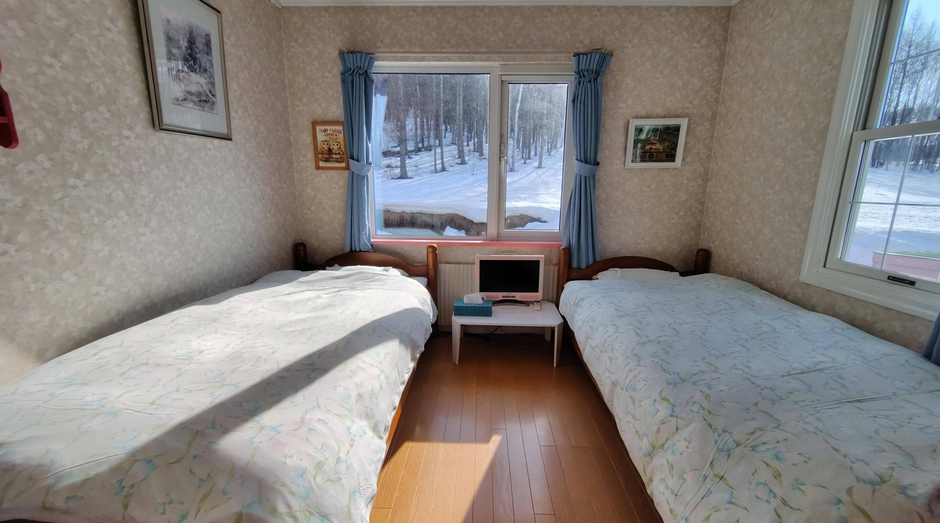 A room with two beds, a small table with a TV, and a window with curtains.