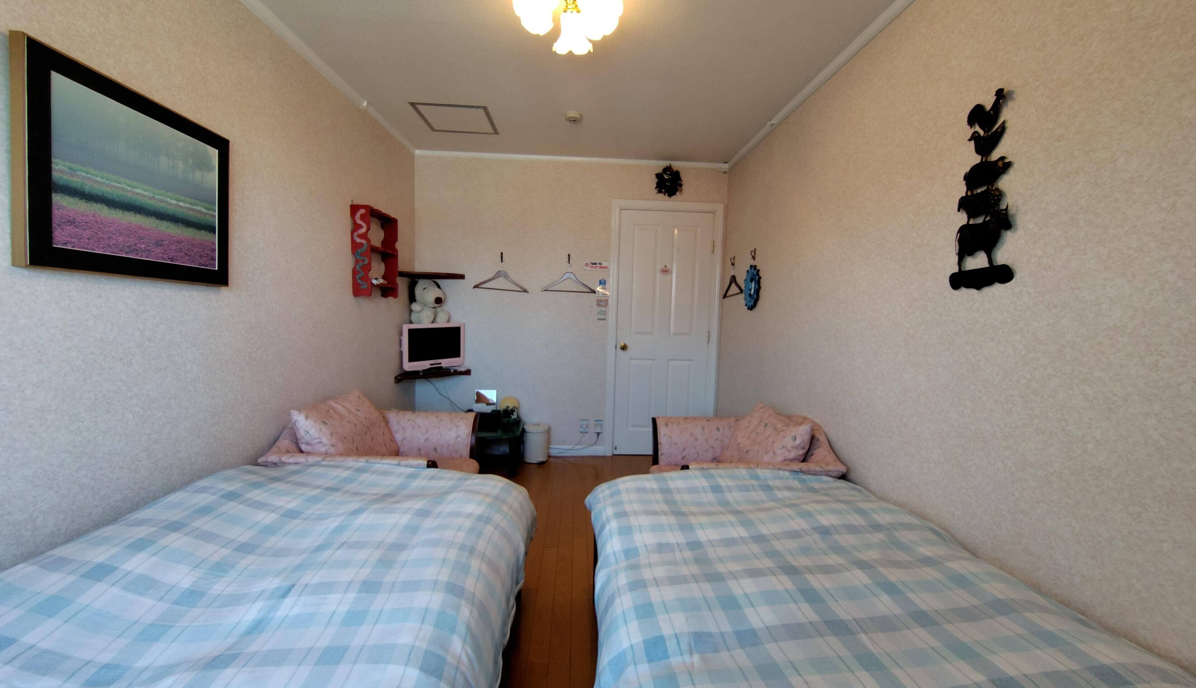 A bedroom with two beds, a TV, a door, and a wall decoration.