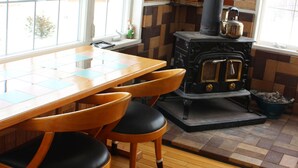A wooden table with chairs, a black stove, and a window with a view of trees. - Pension Hoshi Ni Negaiwo (Furano)