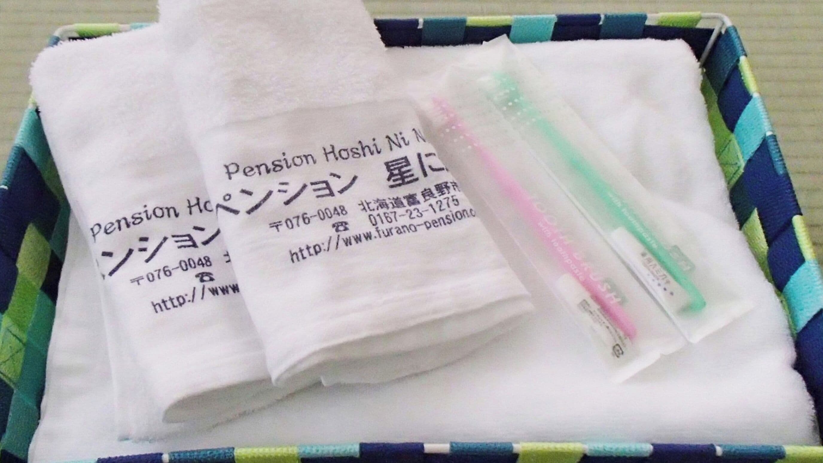 A box containing a white tissue, a pink and green pen, and a white paper with Japanese text.