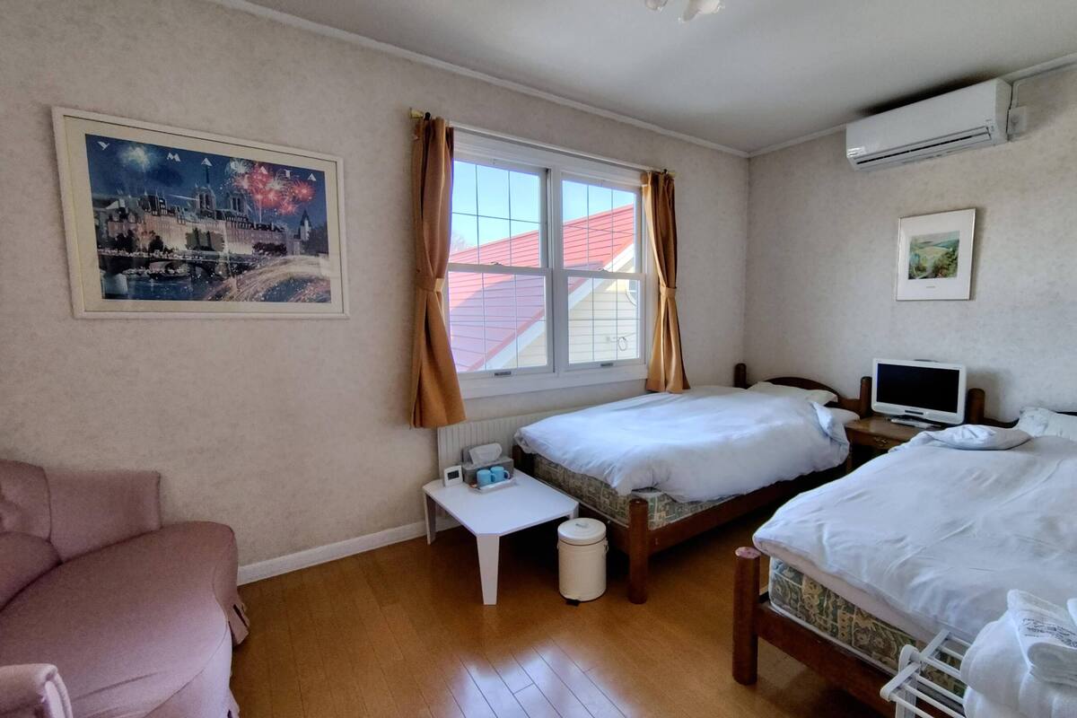 Een slaapkamer met twee bedden, een bureau, een stoel, een televisie en een raam met gordijnen.