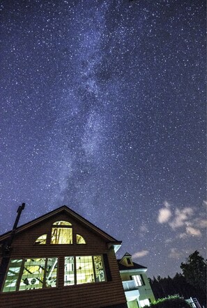 Une maison aux grandes fenêtres, sous un ciel étoilé.