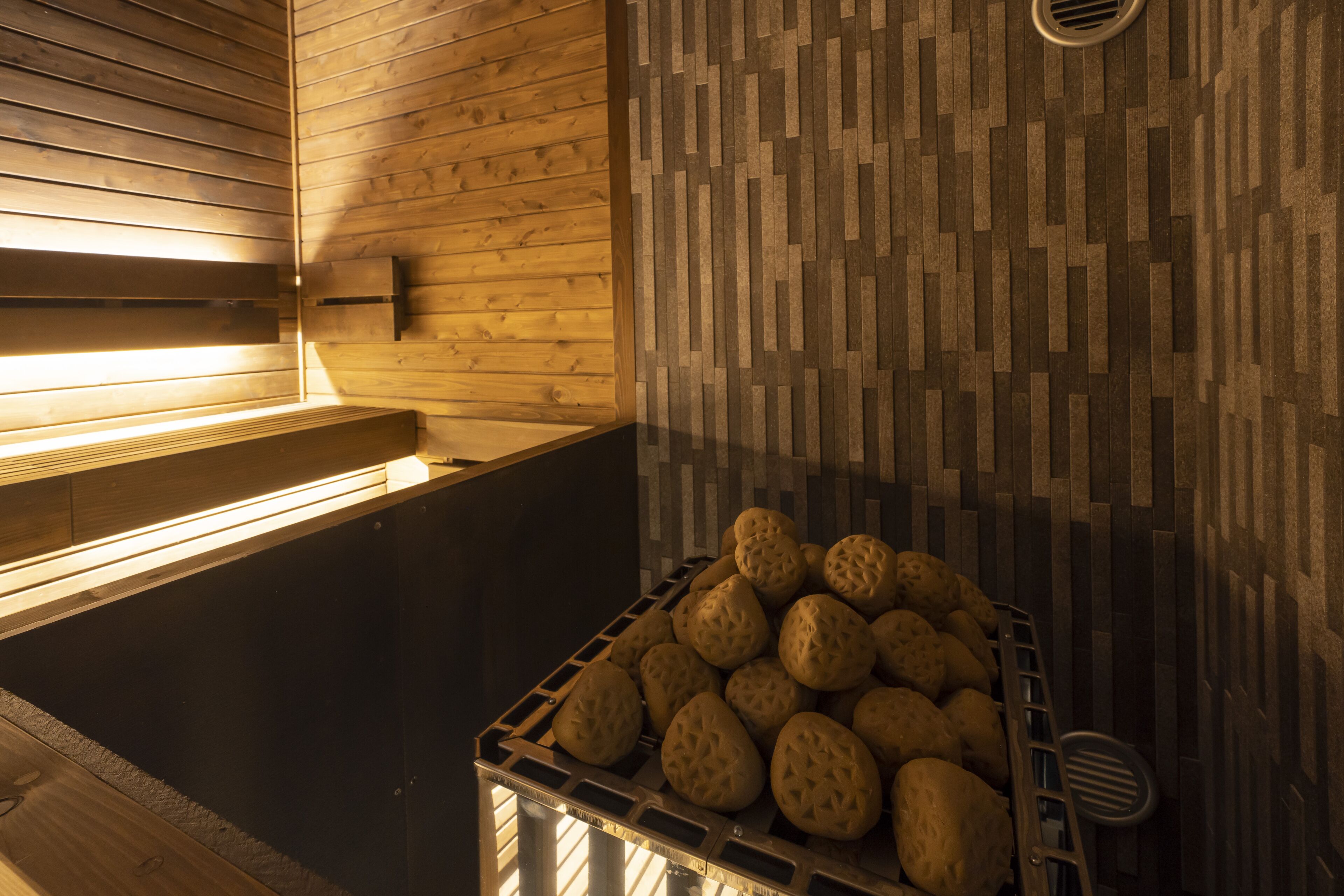 A sauna room with wooden walls, a bench, and a basket of stones.