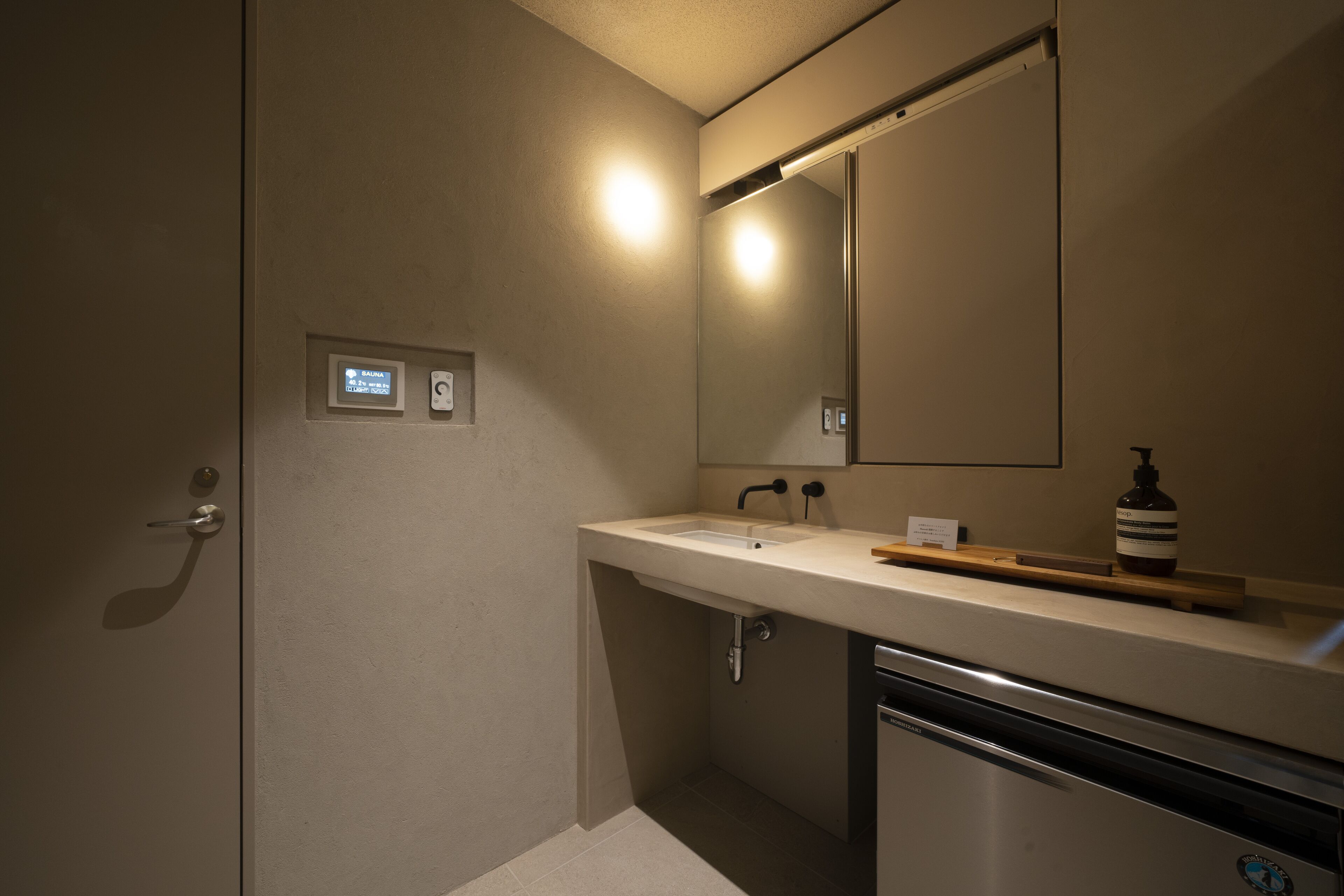 A bathroom with a sink, mirror, and a soap dispenser.