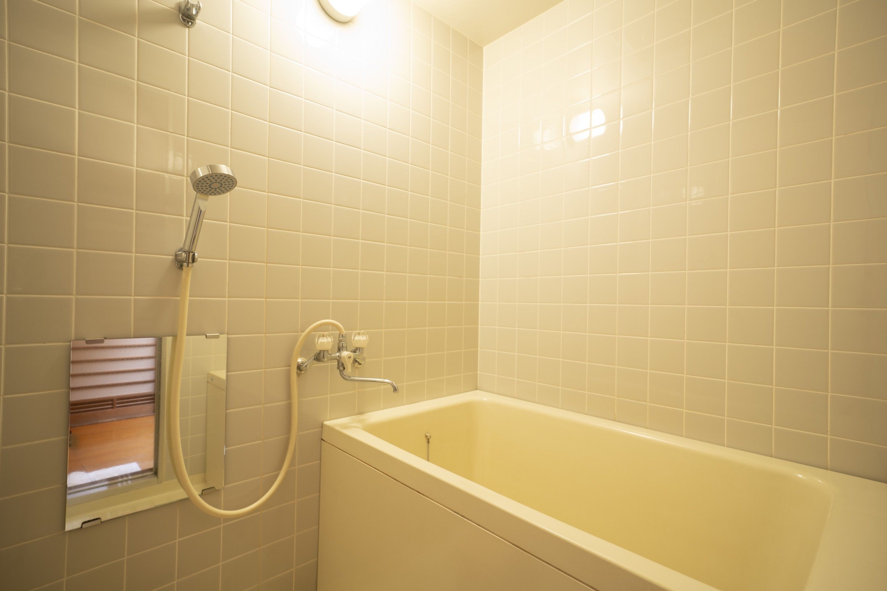 A bathroom with a bathtub, a showerhead, and a window with blinds.