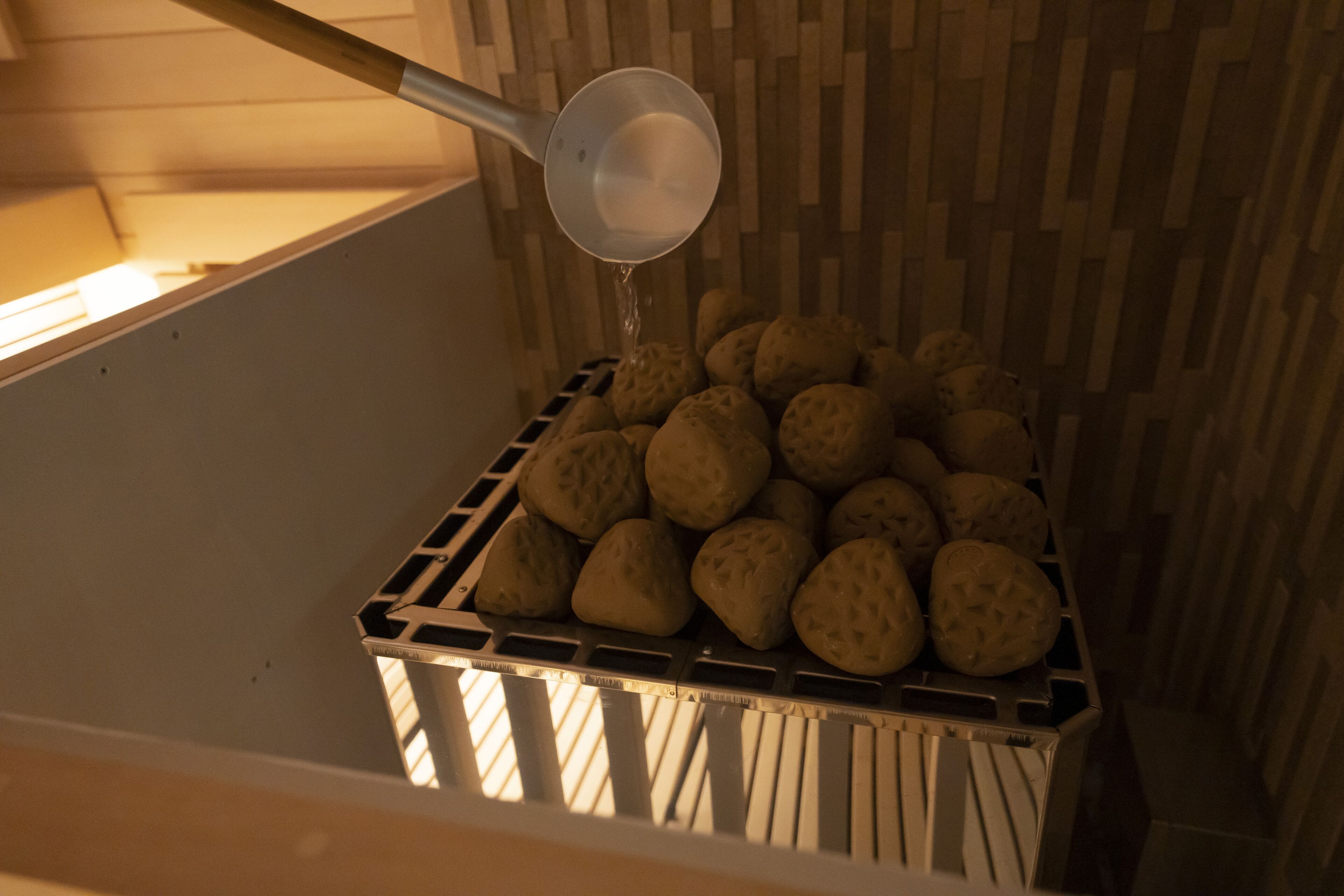 A container filled with round, textured objects, possibly cookies or pastries, with a metal scoop pouring liquid into it.