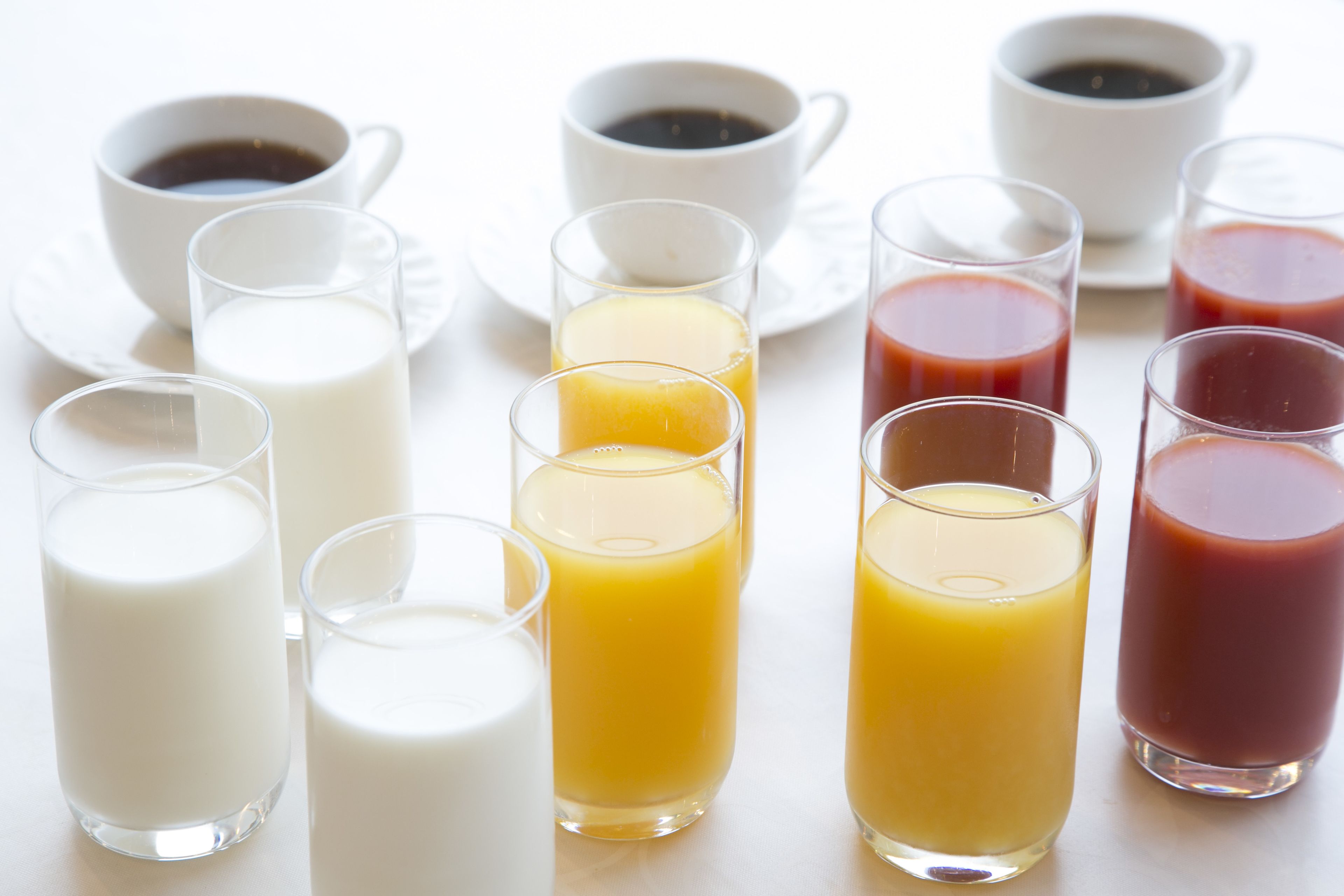 A variety of beverages including milk, orange juice, and coffee in clear glasses on a white table.