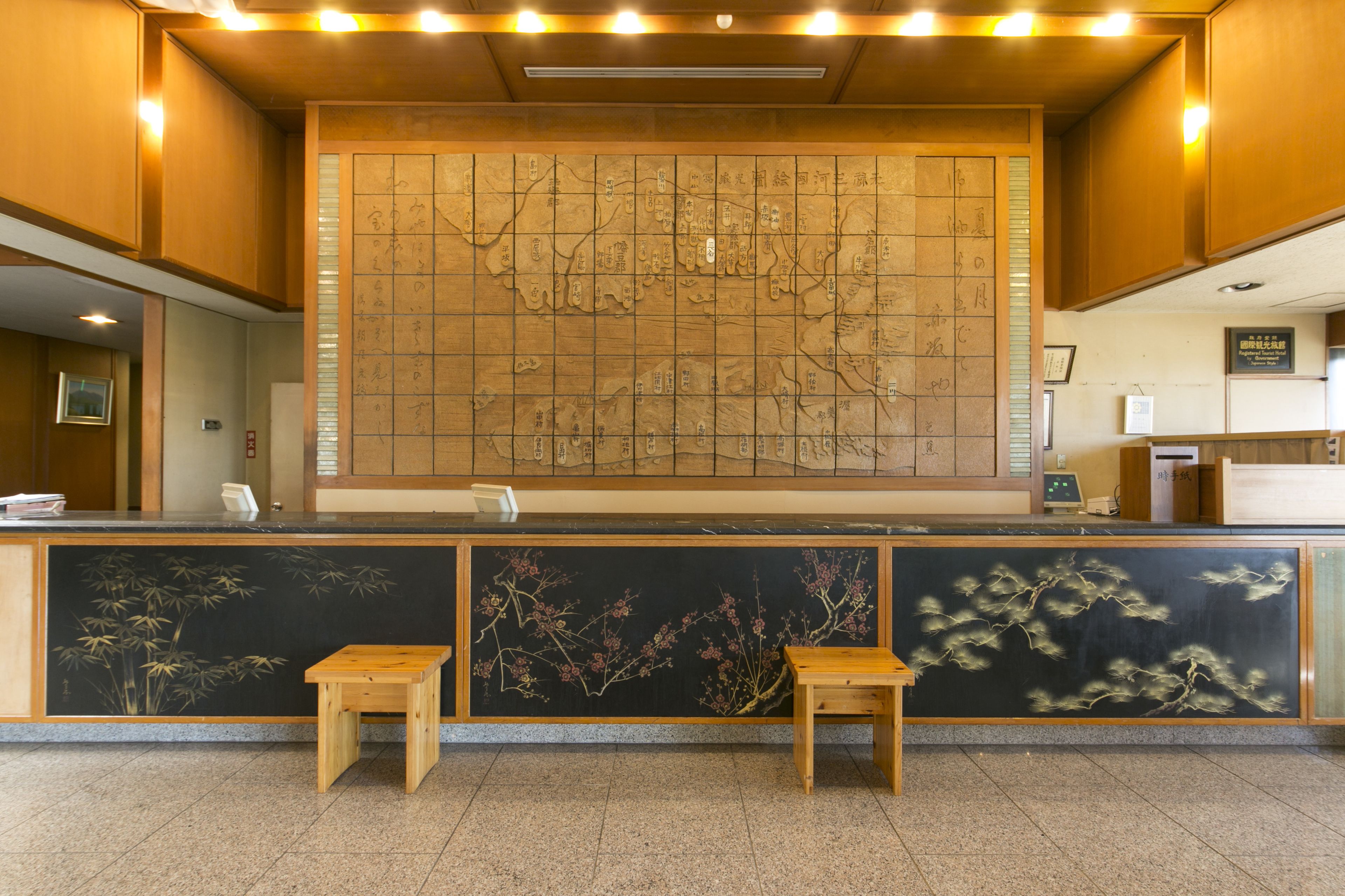 A reception area with a large traditional map mural, two wooden stools, and a reception desk.