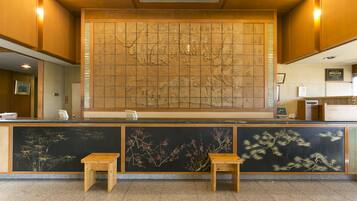 A reception area with a large traditional map mural, two wooden stools, and a reception desk.