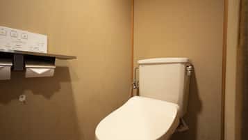 Ein kleines, sauberes Badezimmer mit Toilette, einem Ablagefach mit Papierrollenhalter und einem an der Wand montierten Spülhebel.