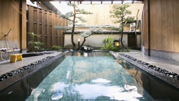 A serene indoor pool with a wooden deck and stone accents, surrounded by wooden walls and potted plants. - Hiranoya (Gamagori)