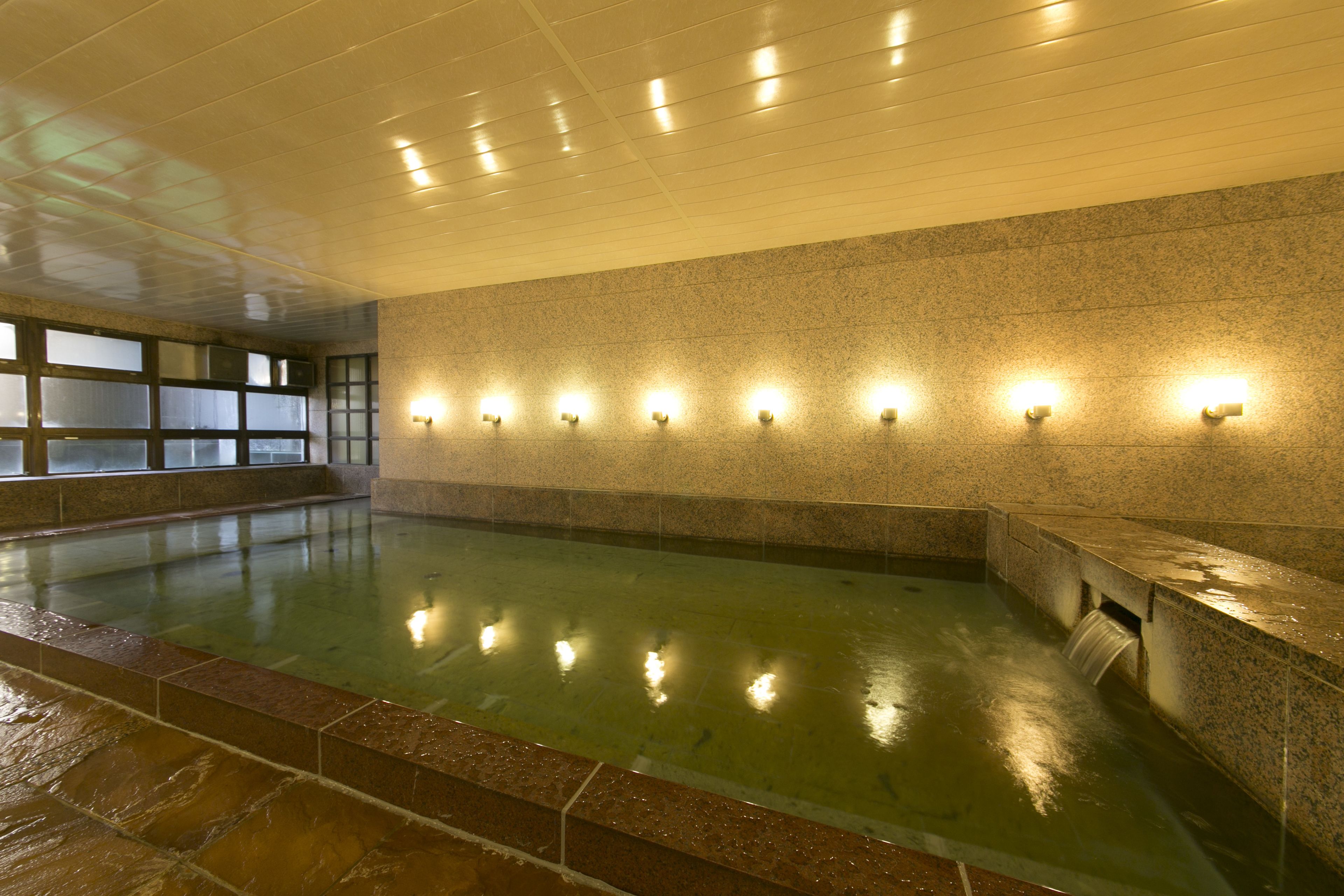 A large indoor swimming pool with a tiled floor and walls, surrounded by benches and illuminated wall sconces.