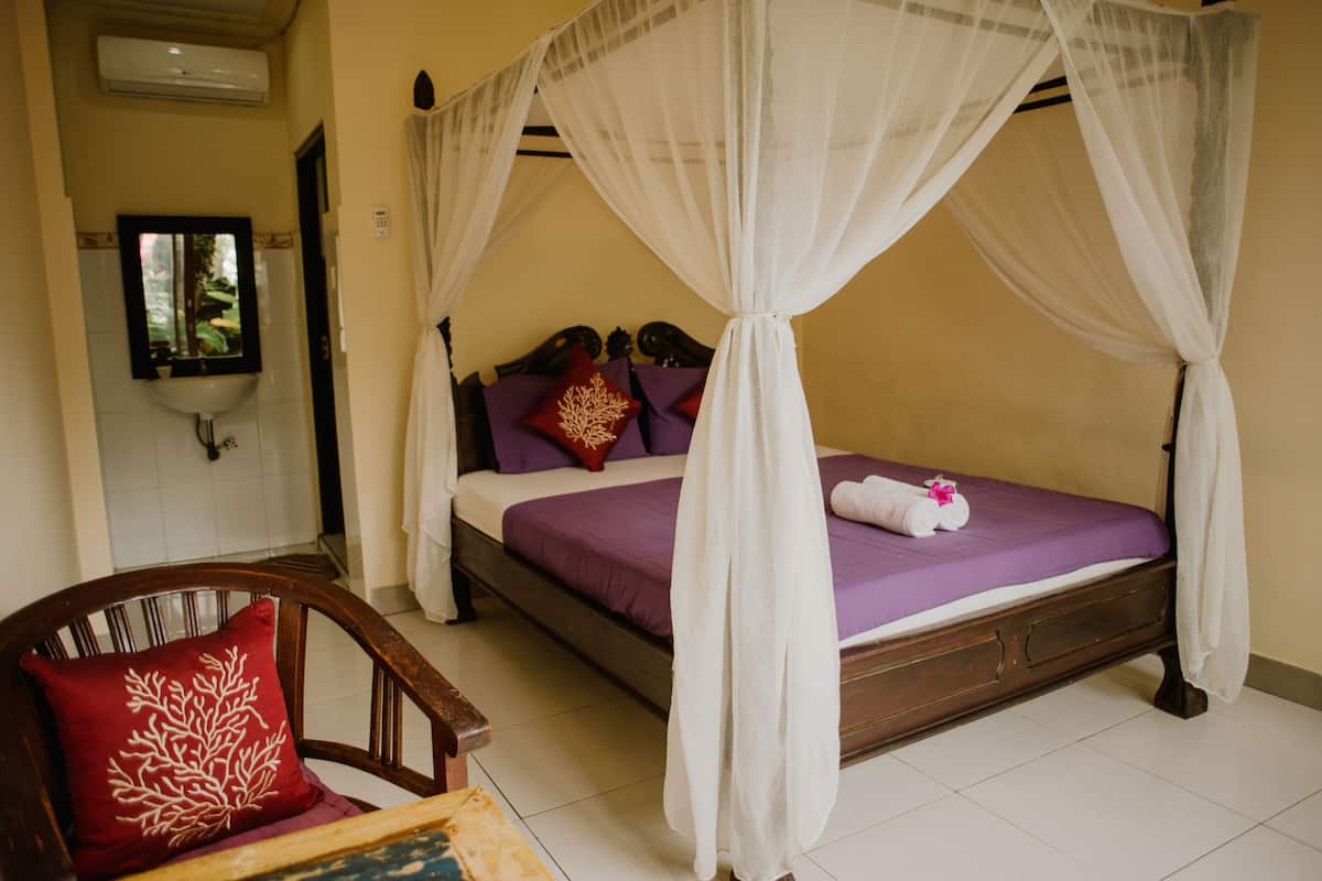 A bedroom with a four-poster bed, a wooden chair, and a red pillow.