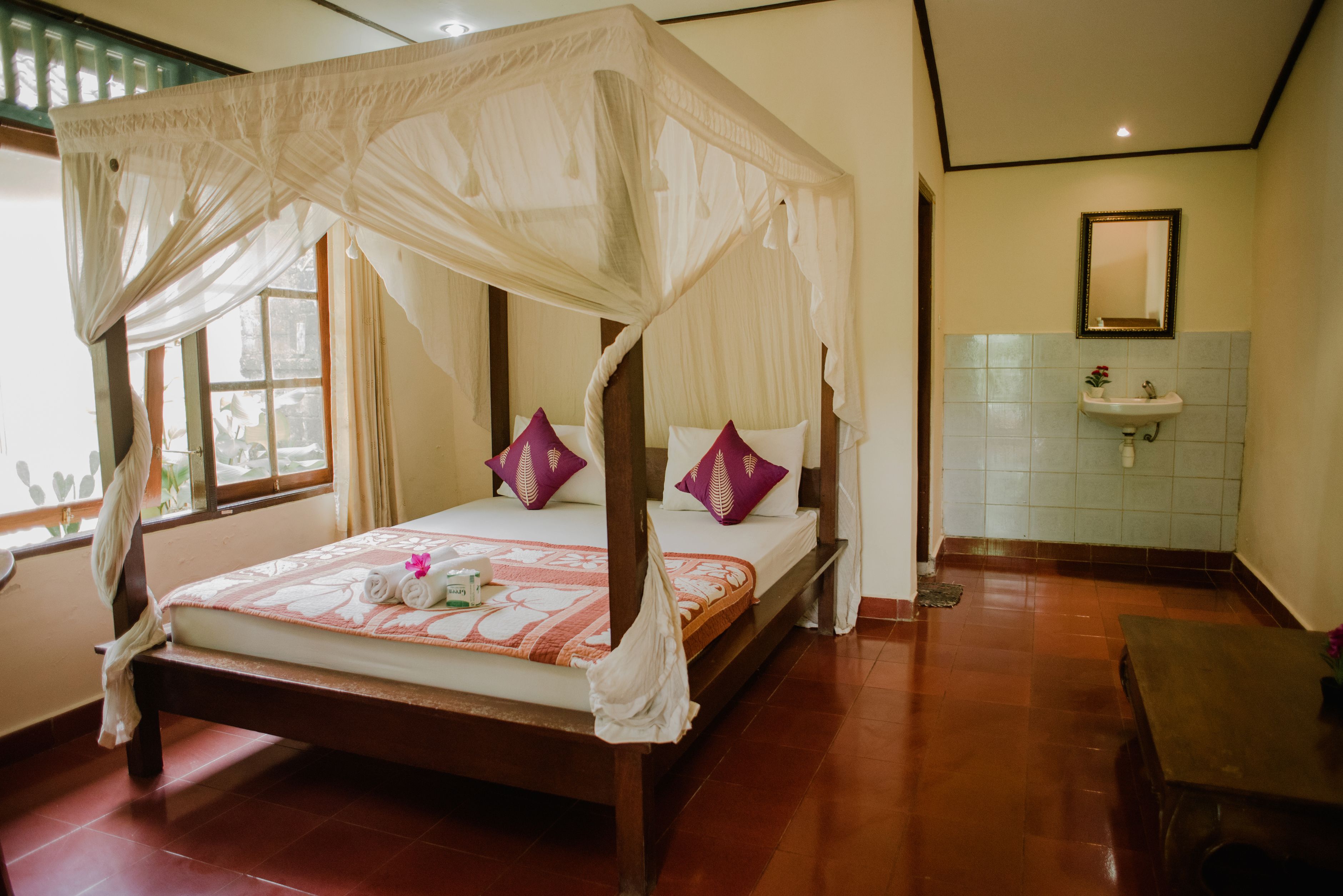 Una cama con dosel, un lavamanos y un espejo en una habitación con paredes de azulejos y piso de madera.