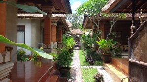 A courtyard with a tiled pathway, potted plants, and traditional architecture. - Nyoman Warta Accommodation (Ubud)