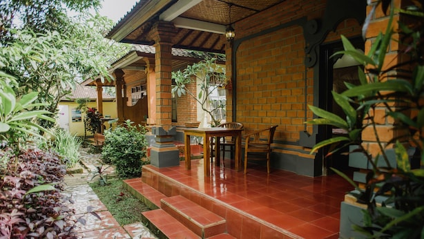 A covered outdoor area with a wooden table and chairs, a brick wall, and a tiled floor. - Nyoman Warta Accommodation (Ubud)