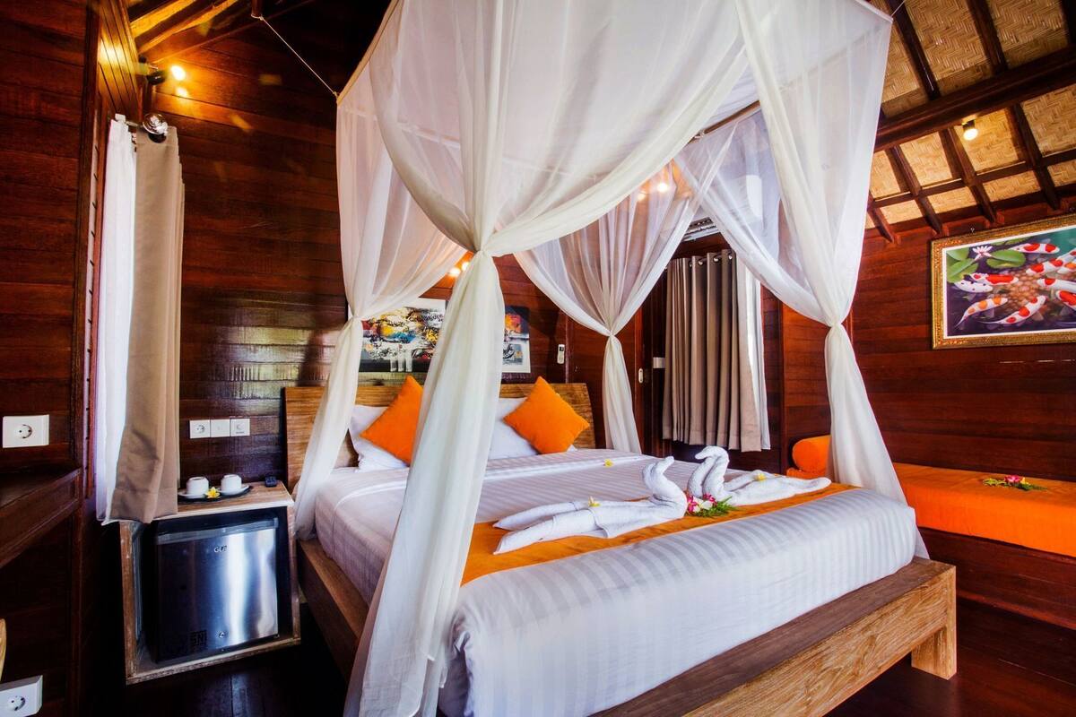A four-poster bed with white linens, orange pillows, and a canopy.