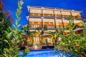 A multi-story hotel with a pool area, outdoor seating, and lush greenery.
