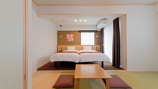 A hotel room with two beds, a wooden table, tatami mats, a window with curtains, and a wall-mounted air conditioner. - M’s Inn Higashiyama (Kyoto)