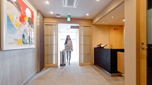 A hotel lobby with a reception desk, a large poster on the wall, and a tiled floor. - M’s Inn Higashiyama (Kyoto)
