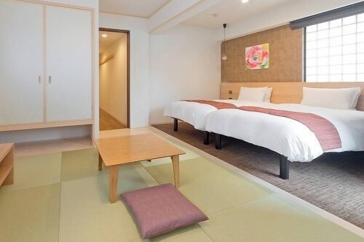 A hotel room with a bed, a small table, a chair, a pillow, and a wall with a painting.