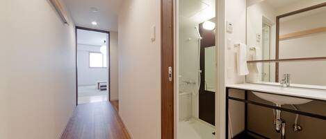 Un baño moderno con piso de madera, cabina de ducha de vidrio y lavamanos blanco con espejo sobre él.