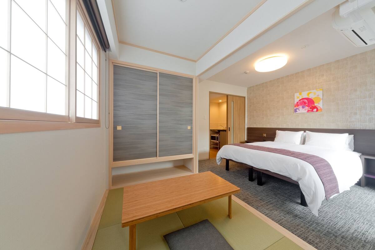 A hotel room with a bed, a wooden table, a sliding door closet, and a wall-mounted air conditioner.