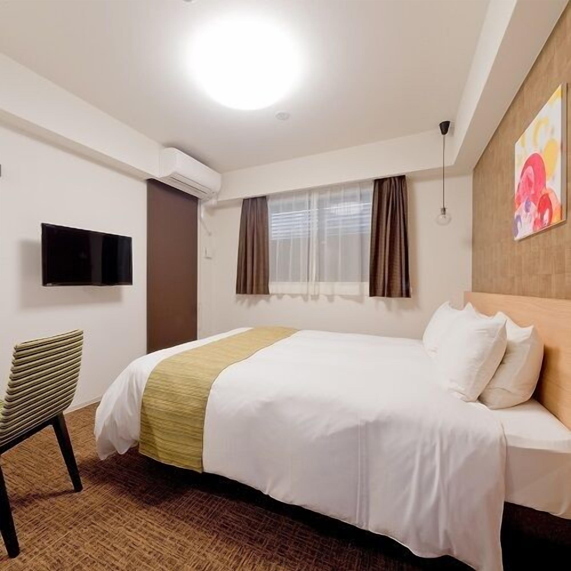 Habitación de hotel con cama, una silla, televisión y ventana con cortinas.
