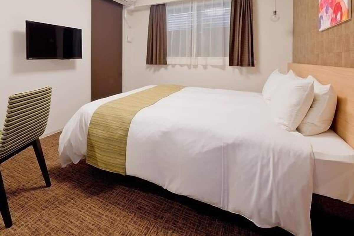 A hotel room with a bed, a chair, a TV, and a window with curtains.