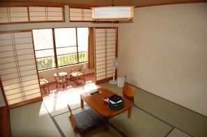 Una tradizionale stanza giapponese con pavimento in tatami, un tavolino con cuscini, una ventaglio e porte scorrevoli shoji.