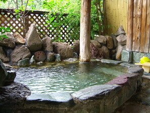 Un giardino roccioso con un piccolo stagno, circondato da bambù e strutture in legno.